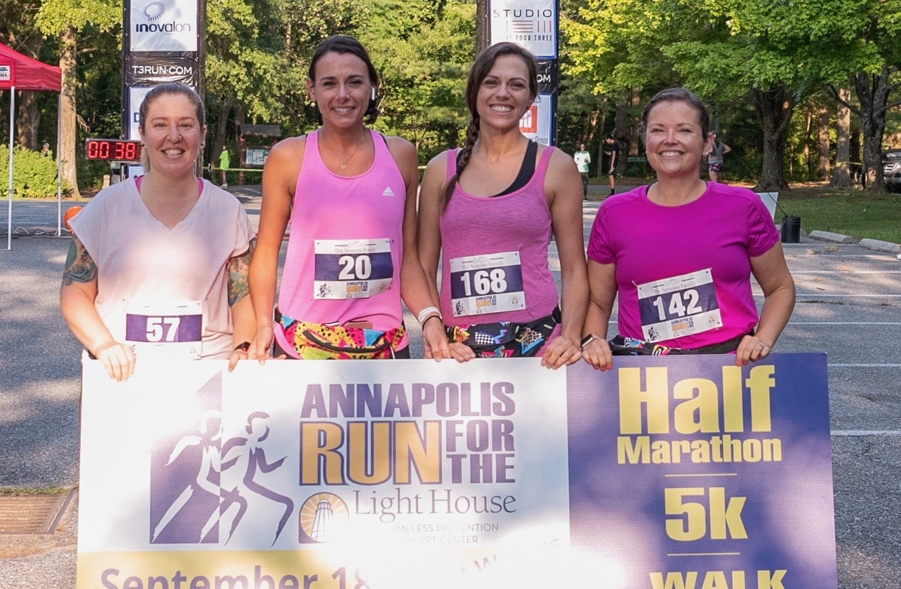 Four women posing with an Annapolis RUN for the Light House sign